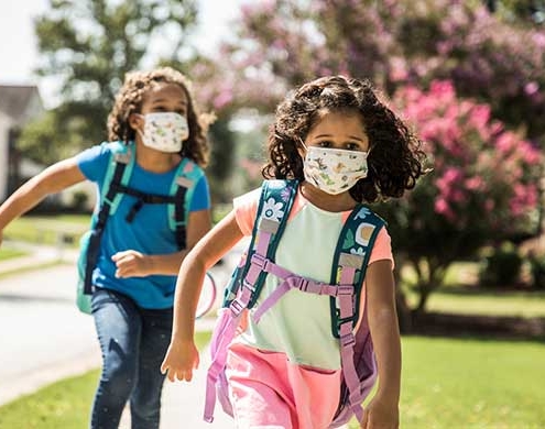 two-girls-running-to-school-wearing-backpacks-and-masks